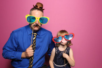 Man and young girl with glasses and props posing with pink backdrop