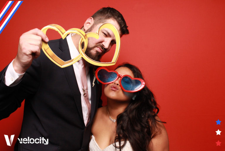 Couple posing with props in front of red backdrop