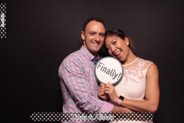 Couple with sign prop posing in front of black backdrop