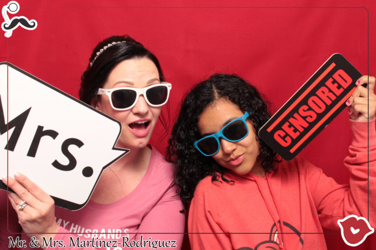 Two women posing with sign props and sunglasses in front of red backdrop