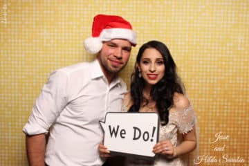 Couple with Christmas hat and we do prop sign posing in front of a gold shimmer backdrop