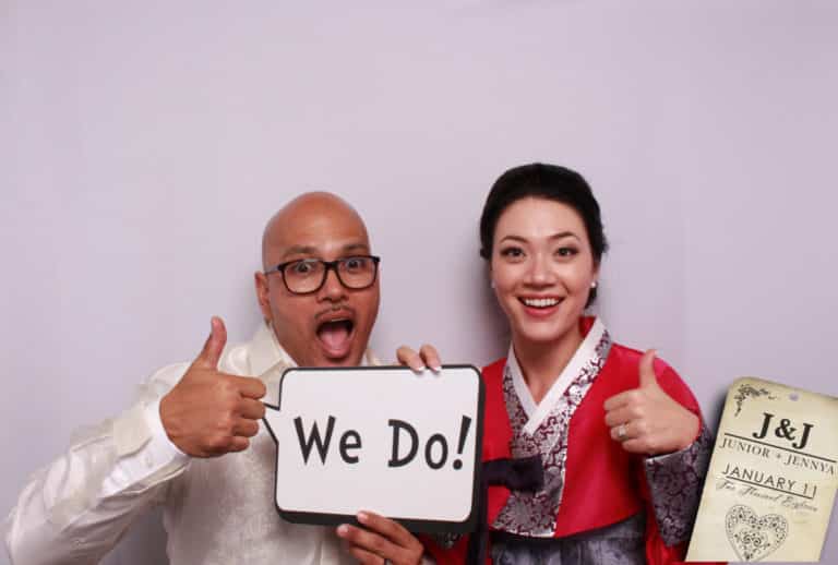 Couple posing with we do prop sign and white backdrop