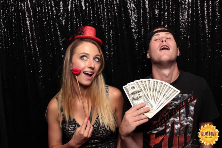 Couple posing in front of a black backdrop with money prop and hat