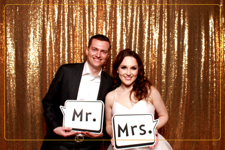Couple posing in front of a shiny backdrop with mr and mrs props