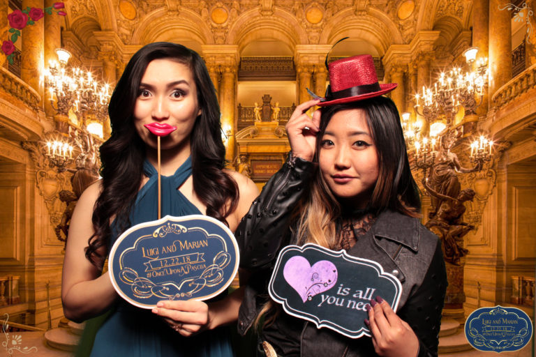 Two women posing with props and hat in front of grand entrance backdrop