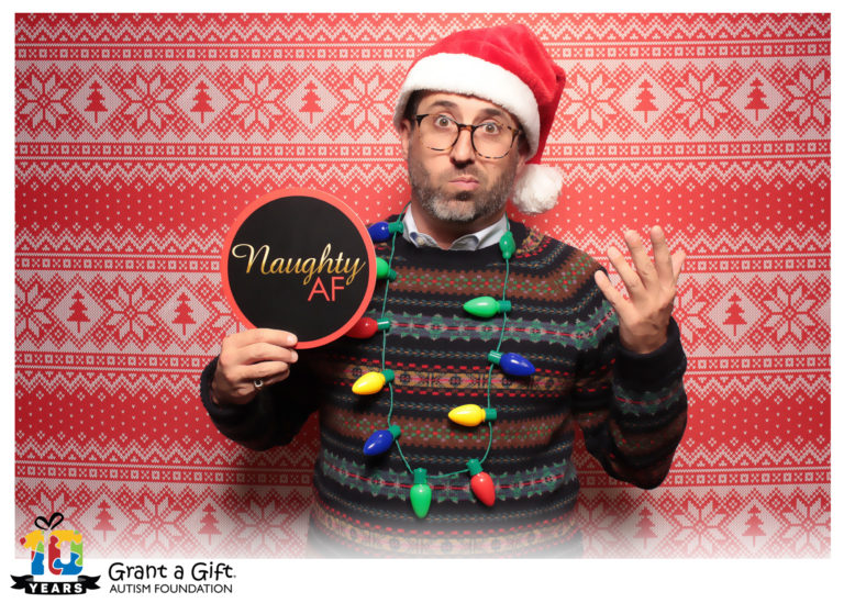 man posing with ugly sweater backdrop and Christmas props