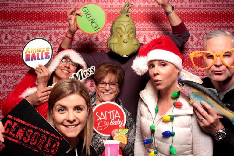 Group posing with ugly sweater backdrop and Christmas props grinch mask