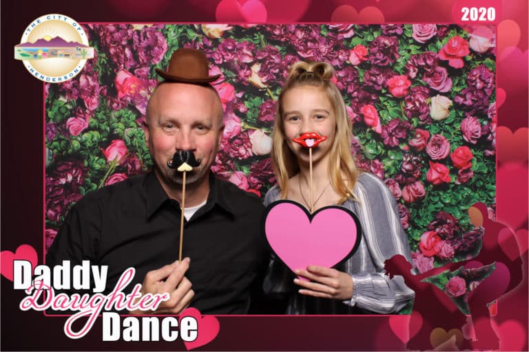 couple posing with rose wall backdrop and pink heart prop