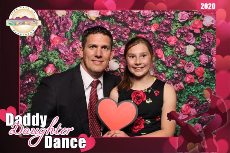 couple posing with rose wall backdrop and red heart prop