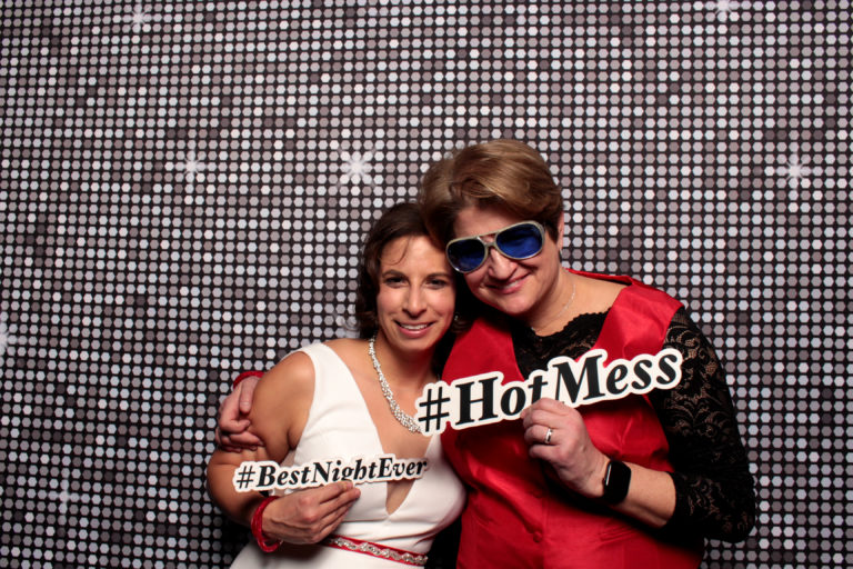 couple posing with silver shimmer backdrop and sign props