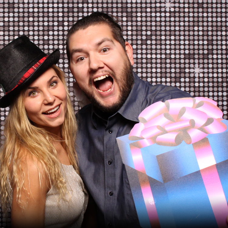 couple posing with silver shimmer backdrop and hat and present prop