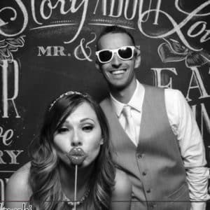 black and white image of couple posing with chalkboard backdrop and props Photo Booth Rentals in Las Vegas Smash Booth