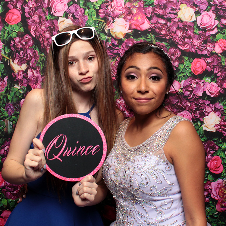 two women posing with rose wall backdrop and sign prop