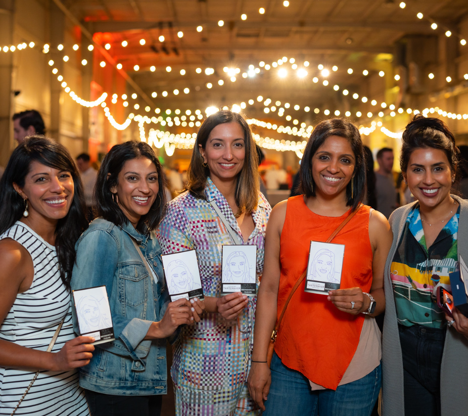 group-of-women-holding-event-programs-under-string-lights-at-smash-booth-booth