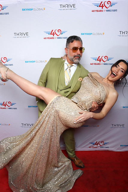man-in-green-suit-holding-woman-in-sequined-gown-at-smash-booth-red-carpet-event