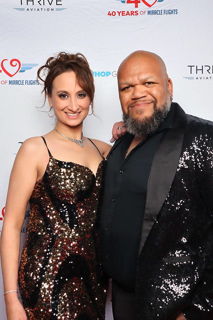 woman-in-sequined-gown-posing-with-man-in-suit-at-smash-booth-event